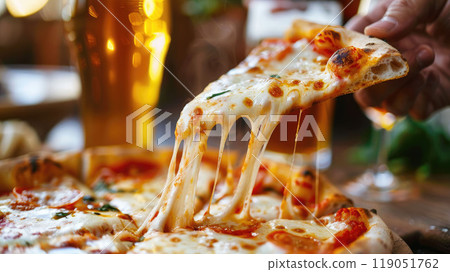 Close-up of a hand lifting a slice of cheesy margherita pizza from a hot, stone-baked pie, with a frosty pint of golden beer in the background. 119051762