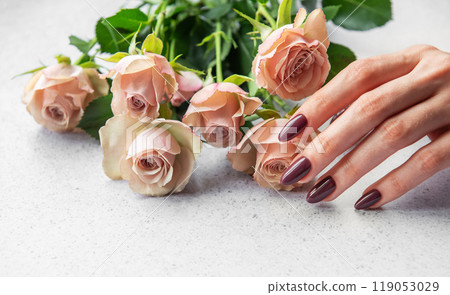 Elegant hand with dark manicure resting beside delicate pink roses on a light surface Elegant hand with dark manicure resting beside delicate pink roses on a light surface 119053029
