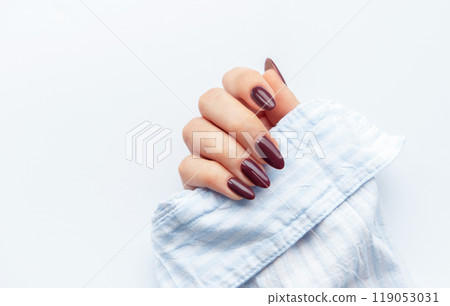 Elegant hand showcasing dark maroon oval nails resting on a light blue fabric Elegant hand showcasing dark maroon oval nails resting on a light blue fabric 119053031