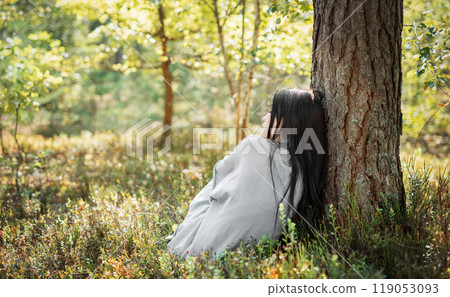 A woman resting against a tree in a serene forest during a sunny afternoon  119053093
