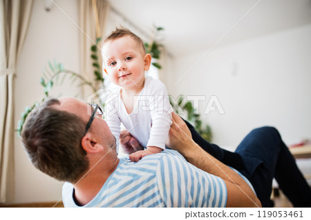 Portrait of father playing with little son, lying on floor and holding small boy above him. Portrait of father playing with little son, lying on floor and holding small boy above him. 119053461