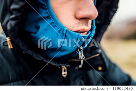 Close-up shot of the face of tourist bundled up in outdoor jacket with hood on. 119053480
