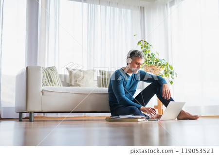 Homeoffice for handsome man. Man sitting on floor and working on laptop with headphones on head. Telecommuting. Homeoffice for handsome man. Man sitting on floor and working on laptop with headphones on head. Telecommuting. 119053521