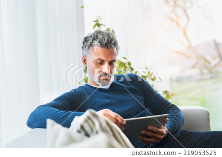 Man at home, watching tv show on tablet, sitting on sofa, feeling cozy. 119053525