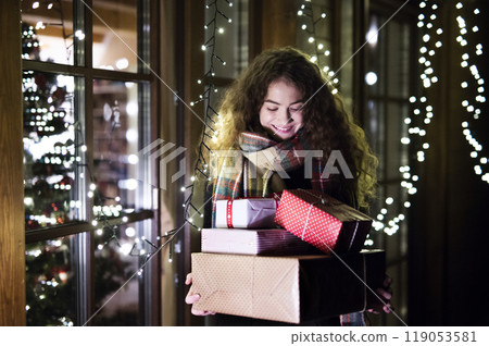 Young woman is shopping for Christmas gifts, carrying a bunch of presents in her hands, walking out of the store. 119053581