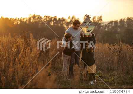 Portrait of young family flying a kite in the autumn nature, jumping in the middle meadow during sunset. Indian summer. 119054784