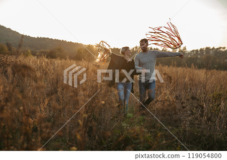 Couple in love on a walk in autumn forest. Husband holding wife hand, holding wreath with ribbons. 119054800