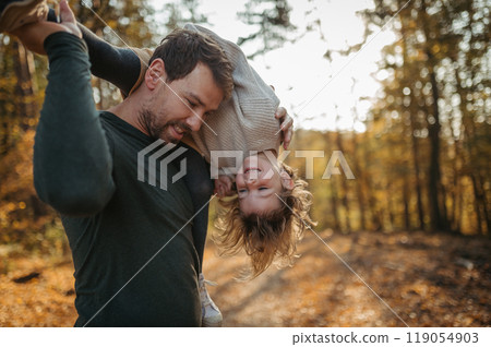 Father and girl are playful during walk in autumn forest. Dad and girl having fun outdoors. 119054903