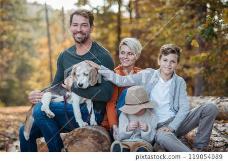 Portrait of family sitting in the middle autumn forest. Nuclear family with dog spending weekend outdoors. 119054989