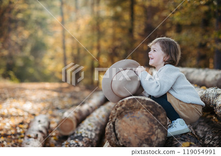 Cute girl with hat sitting on logs in the middle autumn forest, having fun and laughing. 119054991