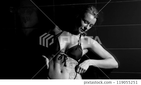 Sexy woman fashion model takes a shower in a swimsuit, posing for the camera. Monochrome photography. Sexy woman fashion model takes a shower in a swimsuit, posing for the camera. Monochrome photography. 119055251