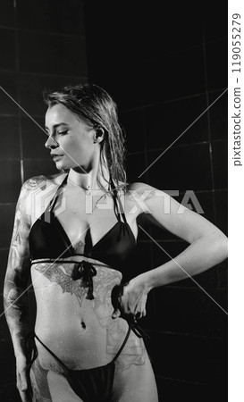 Sexy woman fashion model takes a shower in a swimsuit, posing for the camera. Monochrome photography. Sexy woman fashion model takes a shower in a swimsuit, posing for the camera. Monochrome photography. 119055279
