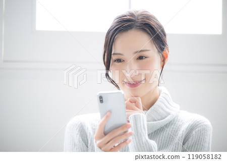 Close-up of a thinking woman wearing winter knitwear tapping on her smartphone. Winter ice blue holding smartphone in hand 119058182