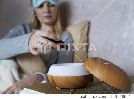 A woman drops essential oils into a humidifier for a restful sleep. Relaxing effect of aromatherapy for anxiety and insomnia. Fighting sleep disorders A woman drops essential oils into a humidifier for a restful sleep. Relaxing effect of aromatherapy for anxiety and insomnia. Fighting sleep disorders 119058665