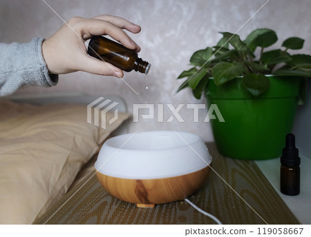 A woman drops essential oils into a humidifier for a restful sleep. Relaxing effect of aromatherapy for anxiety and insomnia. Fighting sleep disorders 119058667