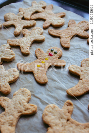 Gingerbread man cookies on baking tray. The only one decorated cookie with smile and eyes. Christmas cookies background. Homemade biscuits. Individuality concept. Cinnamon cookies on baking paper. 119058692