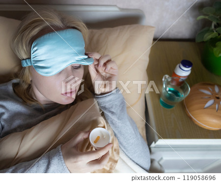 A woman cannot fall asleep and wants to drink a capsule with melatonin, a sleeping pill. Manifestations of jitlag or insomnia. Regulation of biological rhythms 119058696
