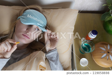 A woman cannot fall asleep and wants to drink a capsule with melatonin, a sleeping pill. Manifestations of jitlag or insomnia. Regulation of biological rhythms 119058698