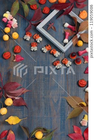 Frame of fall leaves, candy for Halloween. Holidays and food. Dessert in the shape of a pumpkin, skull, witch. Background for design.  119059086