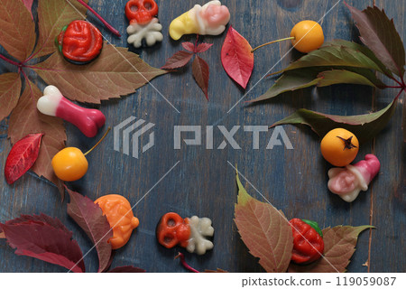 Frame of fall leaves, candy for Halloween. Holidays and food. Dessert in the shape of a pumpkin, skull, witch. Background for design.  119059087