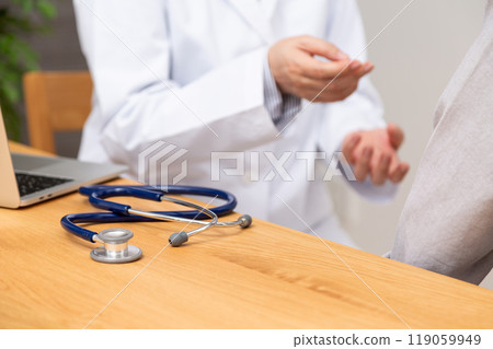 A middle-aged to senior female doctor in a white coat examining a patient A middle-aged to senior female doctor in a white coat examining a patient 119059949