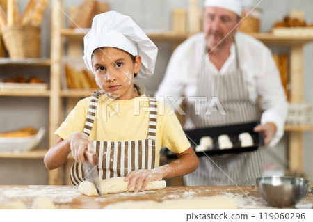 Little girl, baker assistant, cutting raw dough with knife Little girl, baker assistant, cutting raw dough with knife 119060296