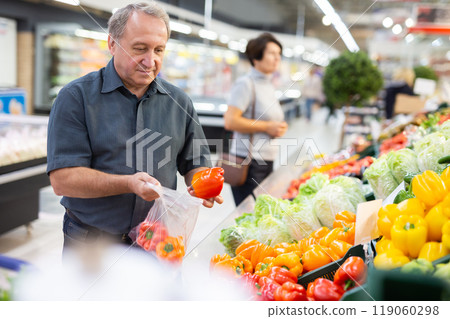 Mature customer selects bell peppers with interest in grocery department of supermarket Mature customer selects bell peppers with interest in grocery department of supermarket 119060298