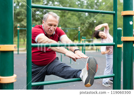 Elderly man doing leg stretching on the outdoor sports ground 119060300
