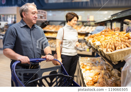 Man takes muffins on shelf of bakery section Man takes muffins on shelf of bakery section 119060305
