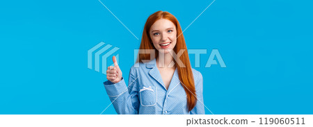 Girl approves recommend product. Cheerful satisfied pretty redhead woman in pyjama, ready sleep, confirm info, showing yes gesture thumbs-up and smiling, standing blue background Girl approves recommend product. Cheerful satisfied pretty redhead woman in pyjama, ready sleep, confirm info, showing yes gesture thumbs-up and smiling, standing blue background 119060511