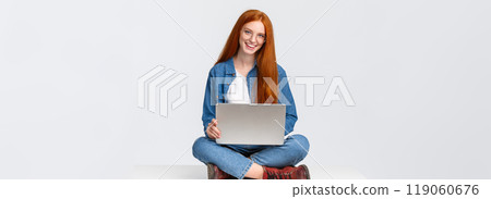 Cheerful sassy redhead female student, college girl in glasses, sitting on crossed legs with laptop, working freelance, prepare project awat from office, remote over white background 119060676