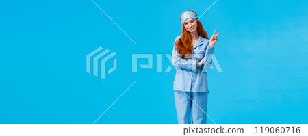 Cute and tender feminine lovely redhead woman in nightwear and sleep mask. Full length vertical studio shot ginger girl in sleeping clothes smiling in morning showing peace sign, blue background Cute and tender feminine lovely redhead woman in nightwear and sleep mask. Full length vertical studio shot ginger girl in sleeping clothes smiling in morning showing peace sign, blue background 119060716