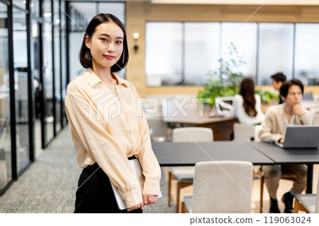 A business person standing and holding a laptop computer, looking straight ahead 119063024