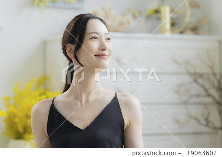 A woman in a black camisole dress standing by the window 119063602