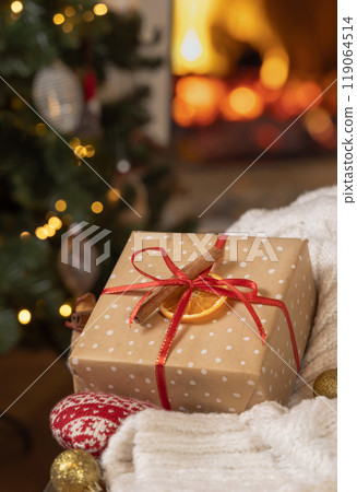 Christmas gift with bow near white sweater against burning fireplace and christmas tree lights 119064514