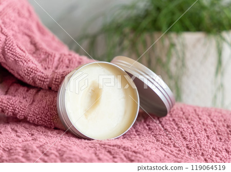 Opened body butter jar on pink towel against green plant close up, herbal cosmetic product Opened body butter jar on pink towel against green plant close up, herbal cosmetic product 119064519