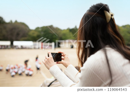 A woman taking pictures of an athletic meet with her smartphone 119064543