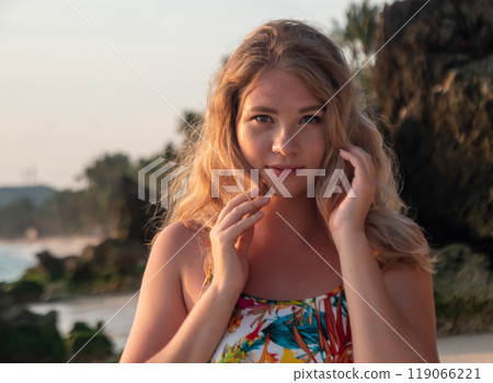 Portrait of a young woman with wavy blonde hair stands at the beach at the sunset. Portrait of a young woman with wavy blonde hair stands at the beach at the sunset. 119066221