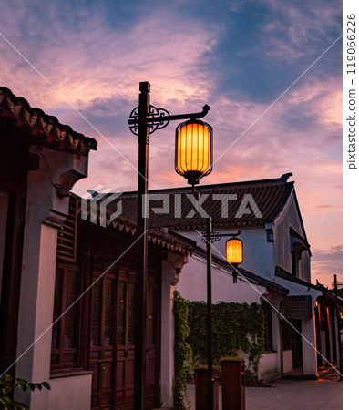 Lanterns glow softly along a quiet Chinese street with traditional buildings as the sun sets, 119066226