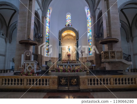 The interior of a church showcases stained glass windows casting colorful light on the altar. Floral arrangements enhance the sacred atmosphere. The interior of a church showcases stained glass windows casting colorful light on the altar. Floral arrangements enhance the sacred atmosphere. 119066280
