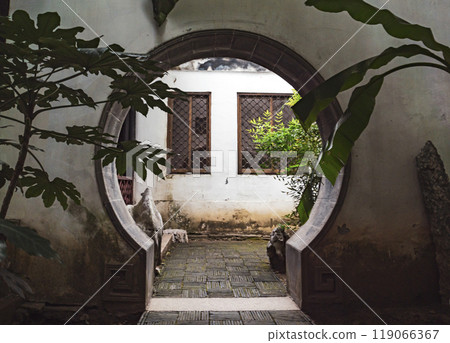 A beautiful circular arch frames a tranquil courtyard filled with greenery in an ancient building A beautiful circular arch frames a tranquil courtyard filled with greenery in an ancient building 119066367