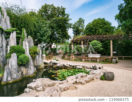 Garden landscape featuring a pond, lush greenery, and carefully arranged rock formations. Garden landscape featuring a pond, lush greenery, and carefully arranged rock formations. 119066375