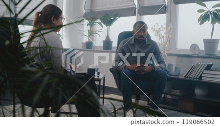 Depressed African American adult man discusses problem with psychologist on counseling session 119066502