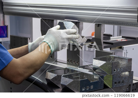 Close up the bending machine operator hold the sheet metal parts with protective glove. 119066619