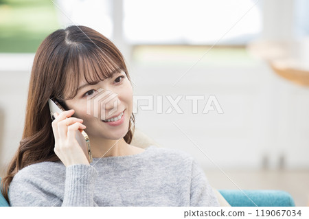 Woman sitting on the sofa and making a phone call Woman sitting on the sofa and making a phone call 119067034