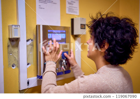 young plus size woman loads clothes into a washing machine in a laundry room in the basement of a student dormitory young plus size woman loads clothes into a washing machine in a laundry room in the basement of a student dormitory 119067090