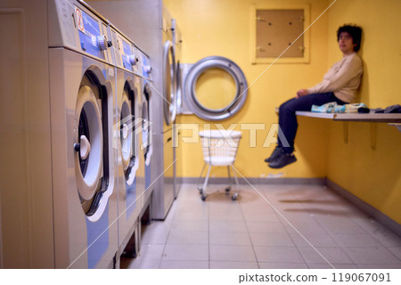 young plus size woman loads clothes into a washing machine in a laundry room in the basement of a student dormitory young plus size woman loads clothes into a washing machine in a laundry room in the basement of a student dormitory 119067091
