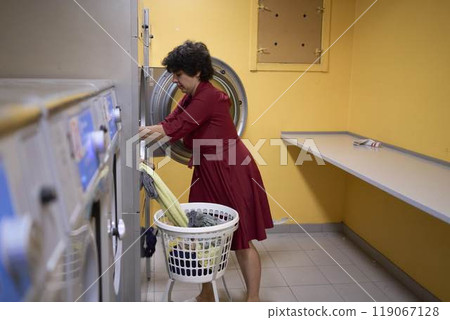 young plus size woman loads clothes into a washing machine in a laundry room in the basement of a student dormitory young plus size woman loads clothes into a washing machine in a laundry room in the basement of a student dormitory 119067128