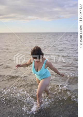 a young plus-size woman is engaged in winter swimming and warming up by the sea a young plus-size woman is engaged in winter swimming and warming up by the sea 119067182