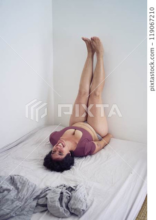 playful young plus size woman in home clothes on bed in student dormitory playful young plus size woman in home clothes on bed in student dormitory 119067210